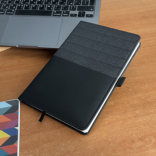 A luxury A5 notebook that is made from a grey fabric and black leather including a pen’s holder.